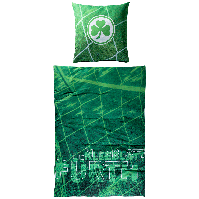 Zweiteiliges Bettwäsche Set in Grün mit Kleeblatt Logo auf dem Kissen und mit „Kleeblatt Fürth“ Schriftzug auf der Decke, im Hintergrund ein Tornetz 